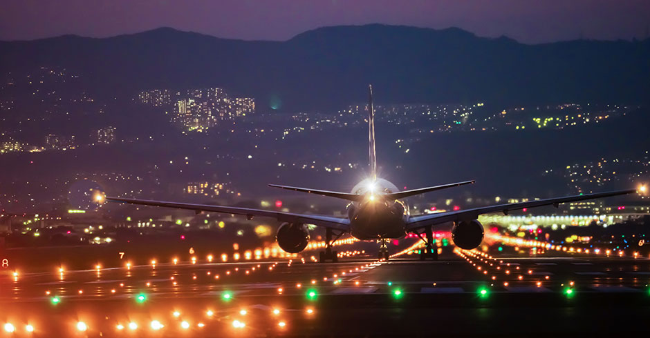 Flugzeug setzt im Abendrot und vor erleuchteter Kulisse zur Landung an | Credit: iStock.com/Takosan