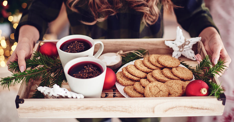 Junge Frau serviert Glühwein auf einem weihnachtlich dekorierten Tablett | Credit: iStock.com/gpointstudio