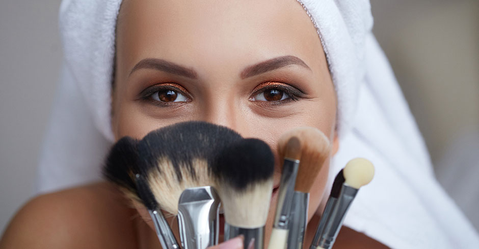 Fröhliche Frau versteckt ihr Gesicht hinter Make-up-Pinseln | Credit: iStock.com/Viktoria Ovcharenko