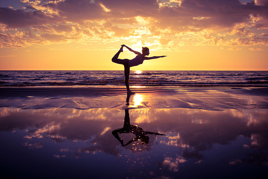 Frau bei ihrem Yoga-Training am Strand bei Sonnenuntergang | Credit: iStock.com/yurok