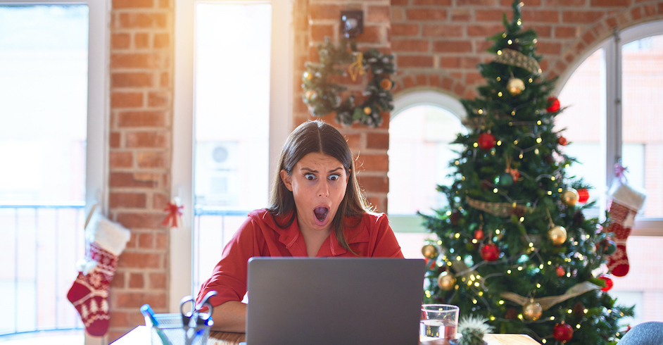 Junge Frau im roten Pullover sitzt am Tisch mit Laptop, dahinter Weihnachtsbaum