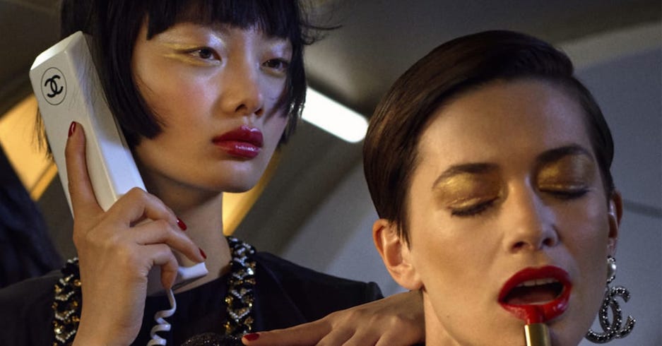 Ein Model hält Telefon ans Ohr, ein zweites schminkt sich die Lippen