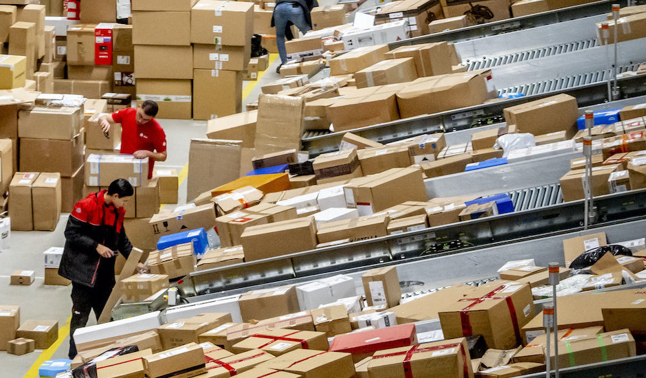 Blick auf mehrere Fließbänder mit zahlreichen Paketen und einem Mitarbeiter