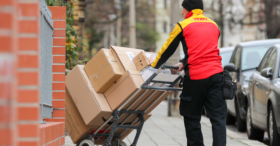 Paketzusteller von hinten fotografiert mit Transportkarre und vielen Paketen