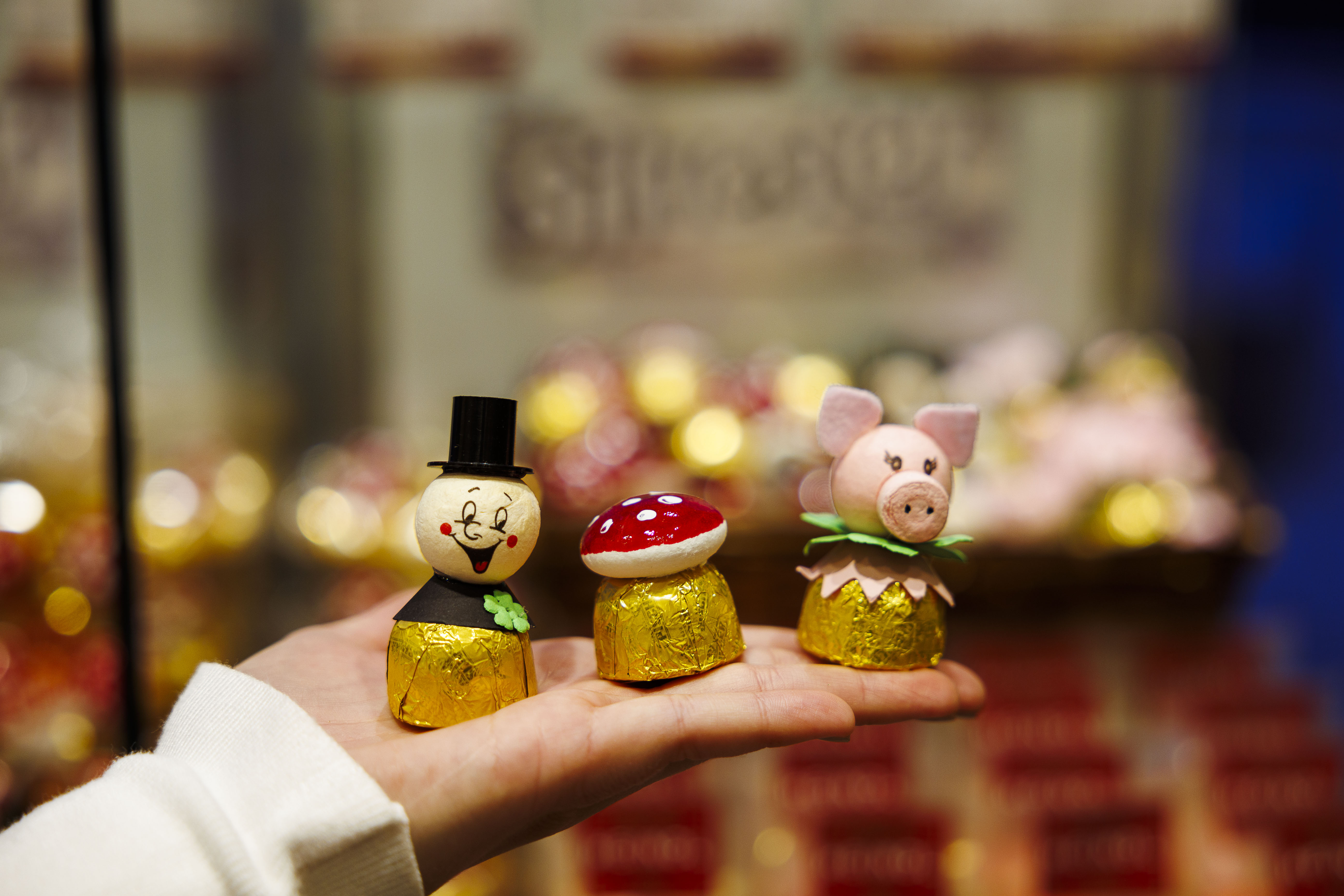 Eine flache Hand hält drei Schokolade-Glücksbringer vor einem Süßigkeitenregal in die Kamera