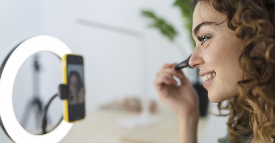 Junge Frau schminkt sich und filmt sich dabei mit dem Handy