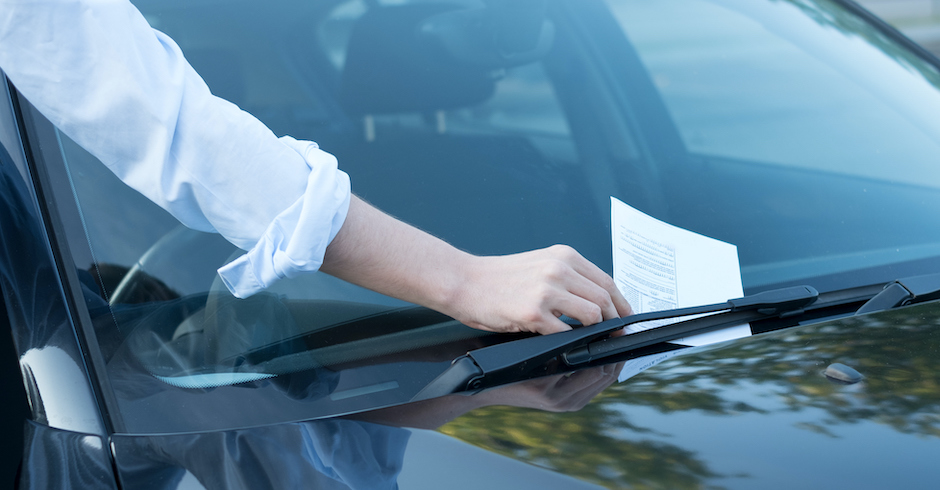 Frau steckt Strafzettel hinter eine Windschutzscheibe | Credit: iStock.com/tommaso79