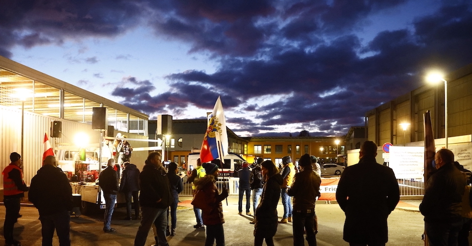 Einzelne Menchen versammeln sich vor der Schule, dahinter Abendhimmel und Wolken