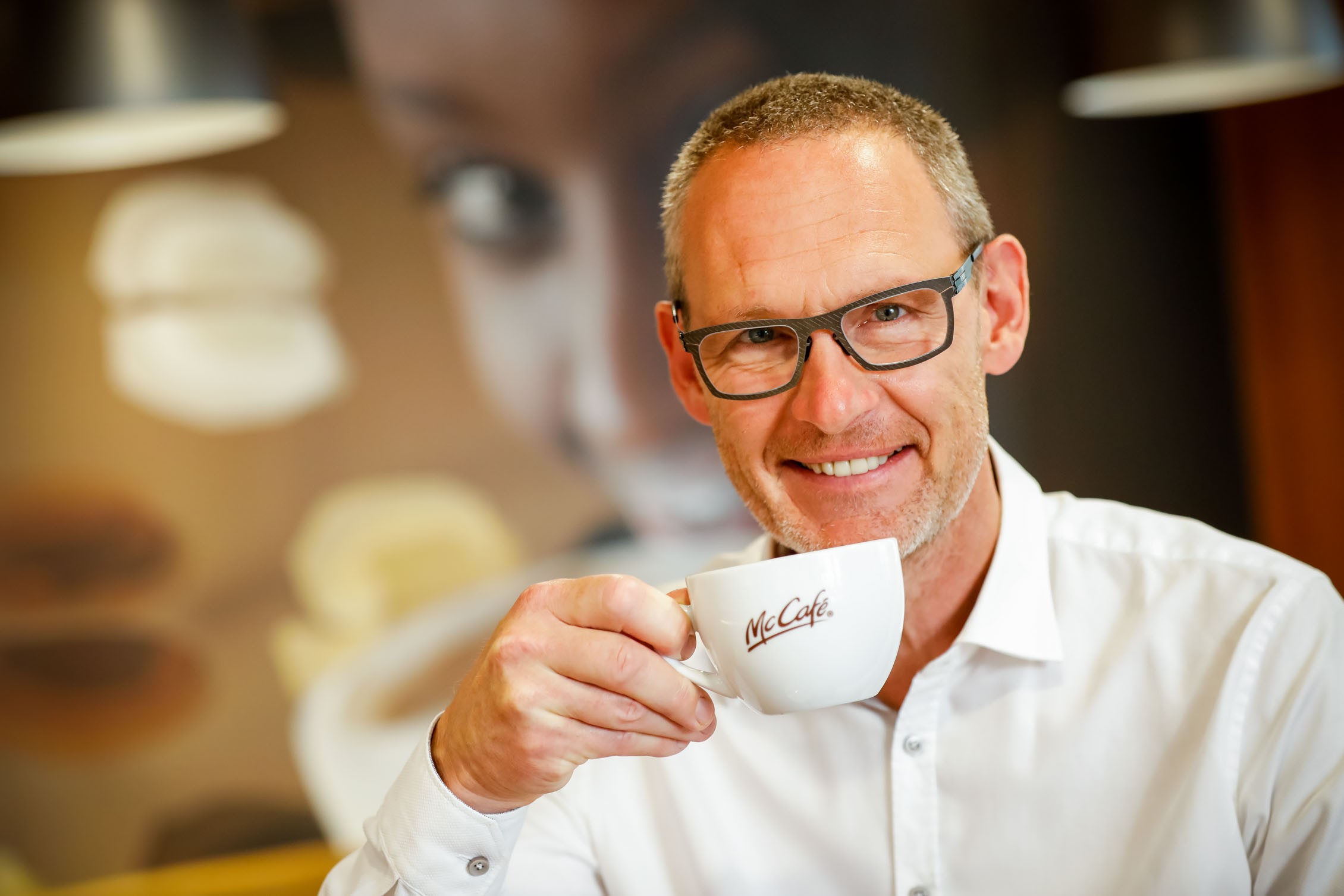 Rudolf Ringhofer führt eine Kaffeetasse mit McCafé-Logo zu seinem Mund