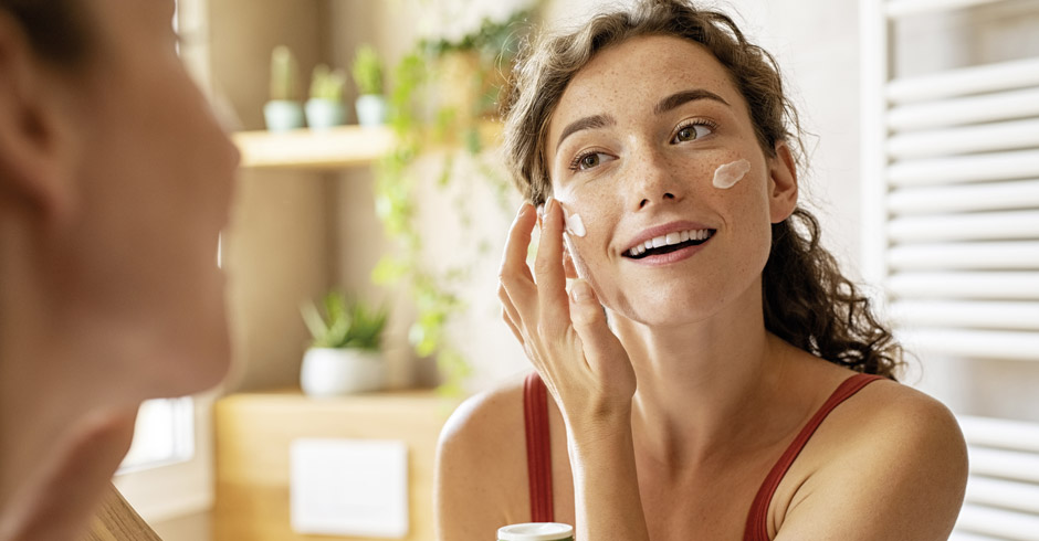 Eine junge Frau die ihr Gesicht eincremt.