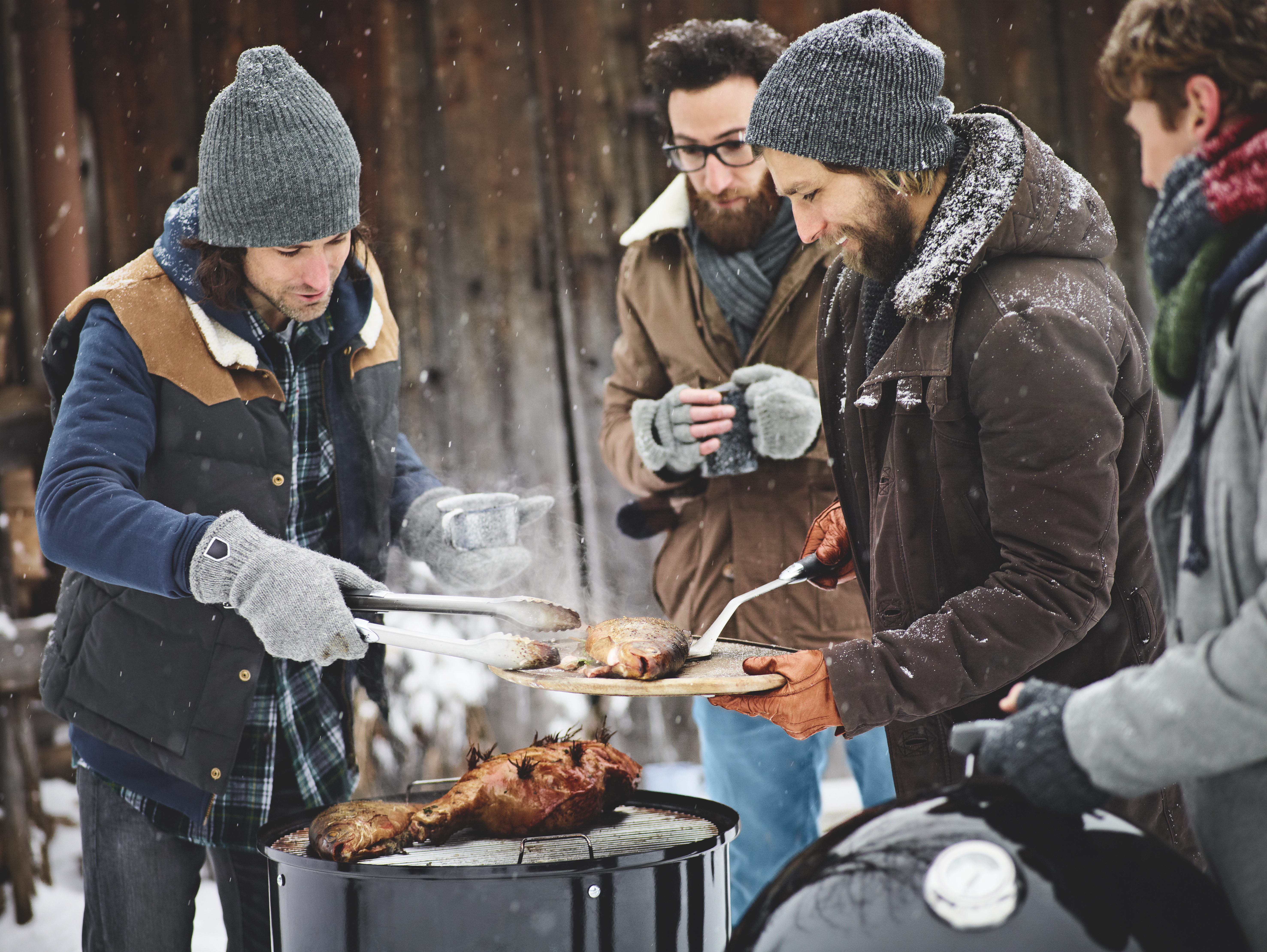 Vier Männer stehen in dicker Wintermontur rund um einen Griller im Freien