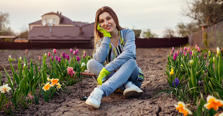 Junge Frau sitzt nach getaner Gartenarbeit entspannt inmitten ihres Blumenbeets | Credit: iStock.com/Maryviolet