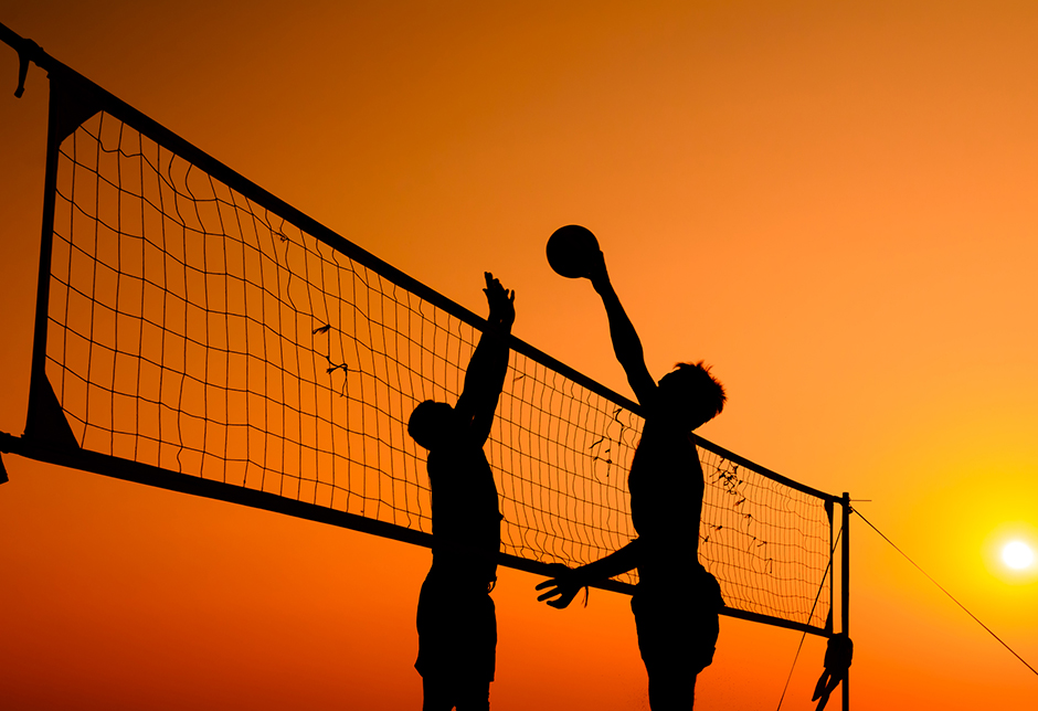 Zwei junge Männer beim Beachvolley bei Sonnenuntergang | Credit: iStock.com/April909
