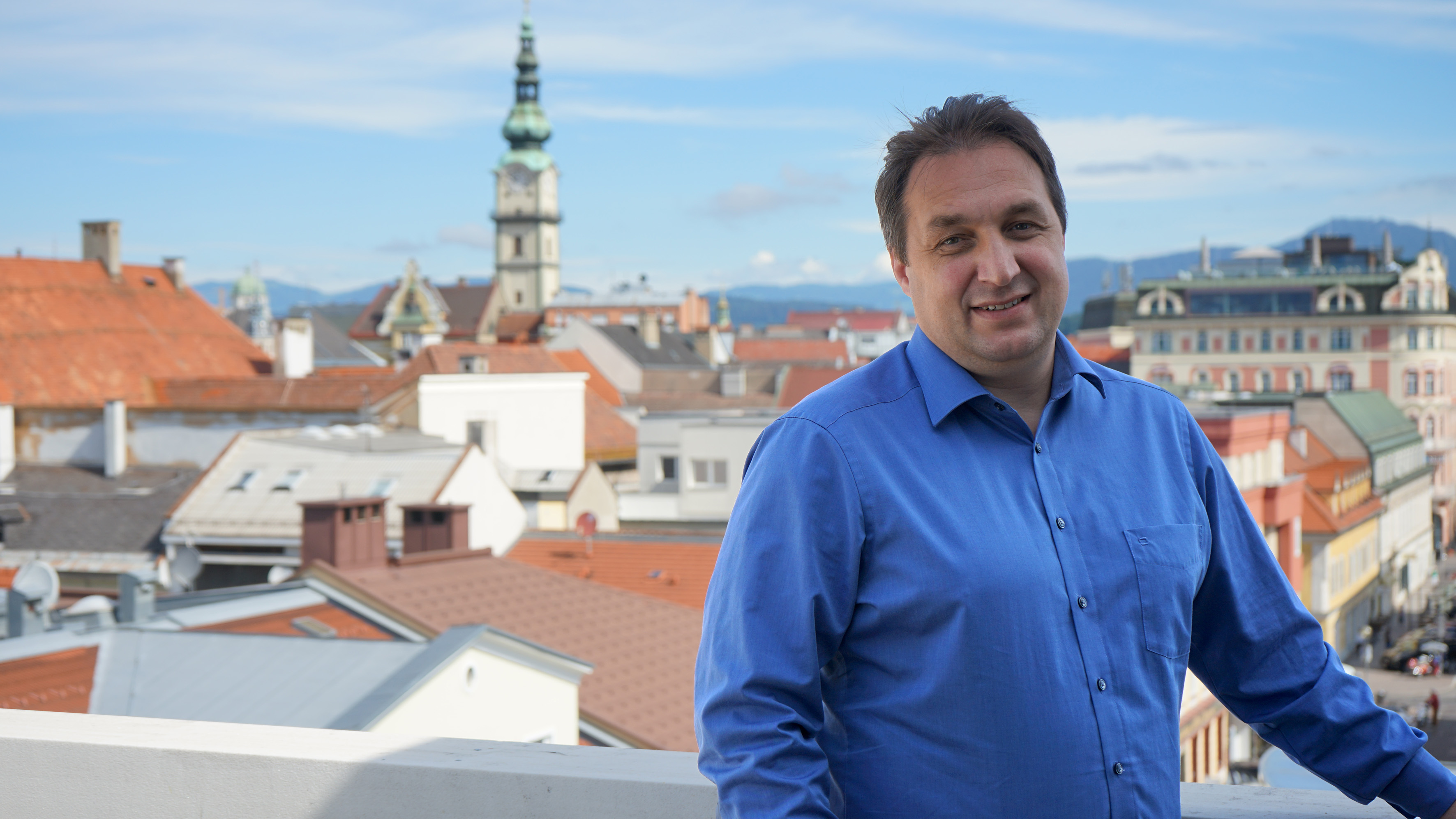 Jürgen Hartinger auf dem Balkon des obersten Stockwerks der KLV-Zentrale vor der Kulisse der Klagenfurter Innenstadt