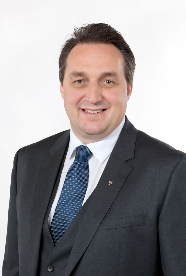 Porträt des Vorstandsdirektors der KLV, Jürgen Hartinger, der einen Anzug samt blauer Krawatte trägt