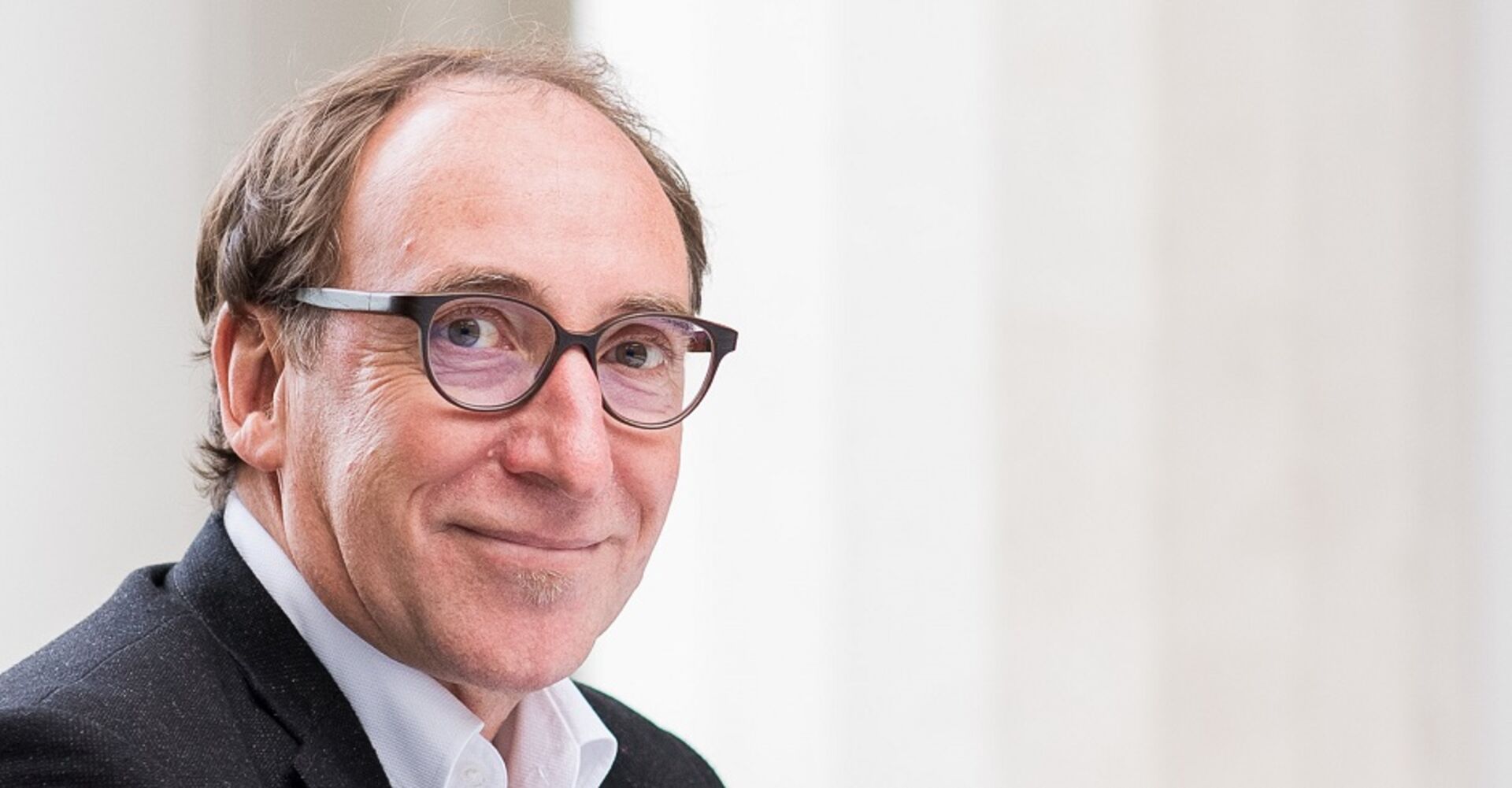 Ein Porträt-Foto von Johnannes Rauch. Er trägt eine Brille mit dunklem Rahmen und schmunzelt in die Kamera.