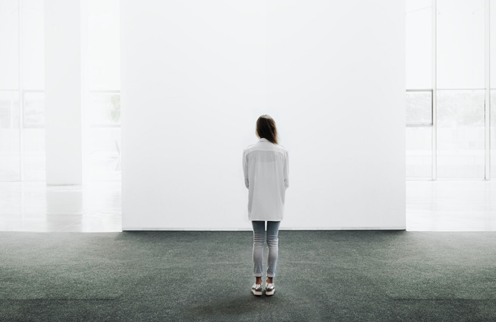 Junge Frau steht vor einer großen, leeren Leinwand in einer Galerie | Credit: iStock.com/Pinkypills