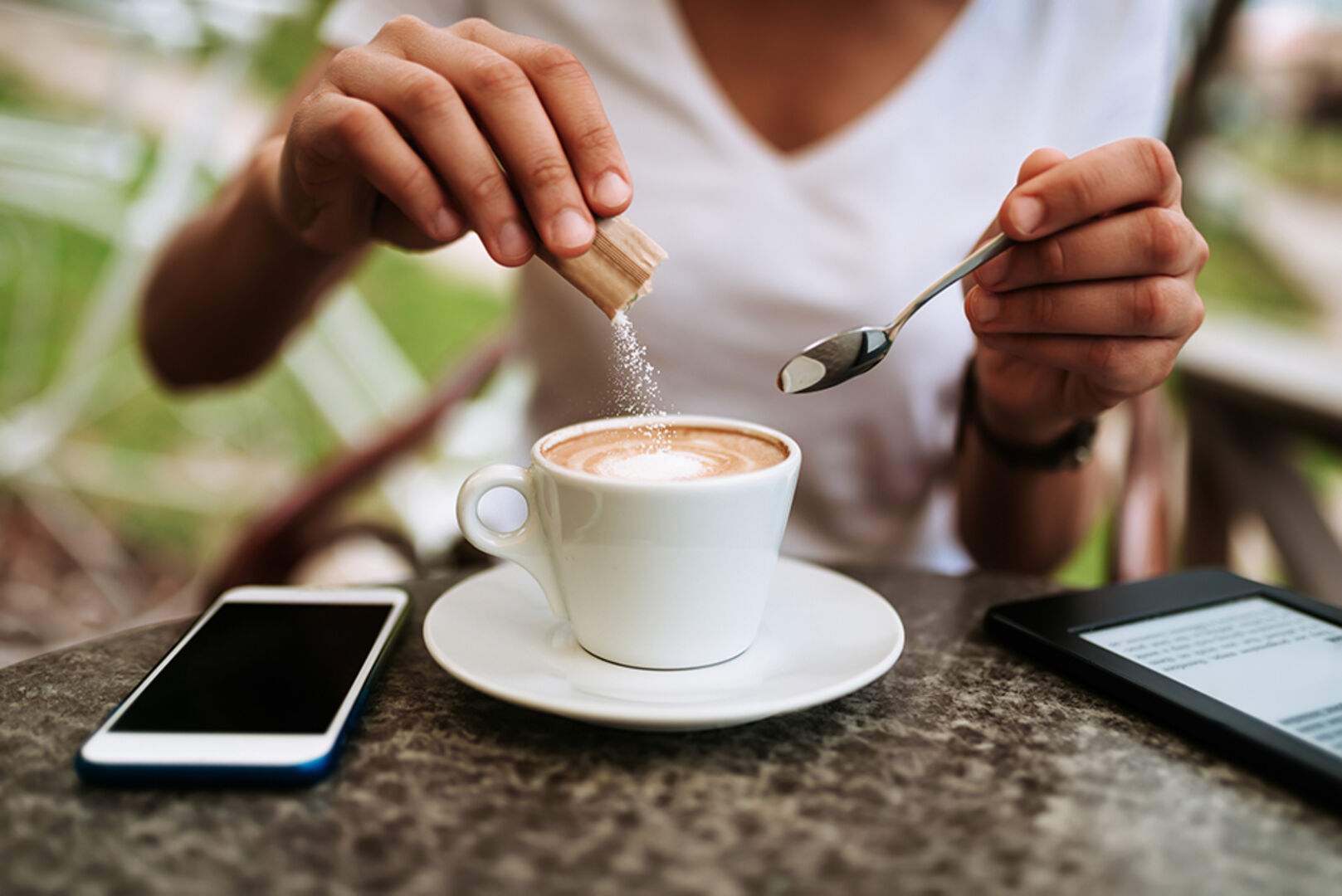 Junge Frau süßt ihren Cappuccino mit weißem Zucker | Credit: iStock.com/nortonrsx