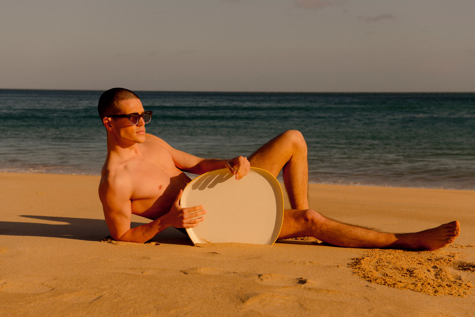 Mann liegt mit Sonnenbrille am Strand