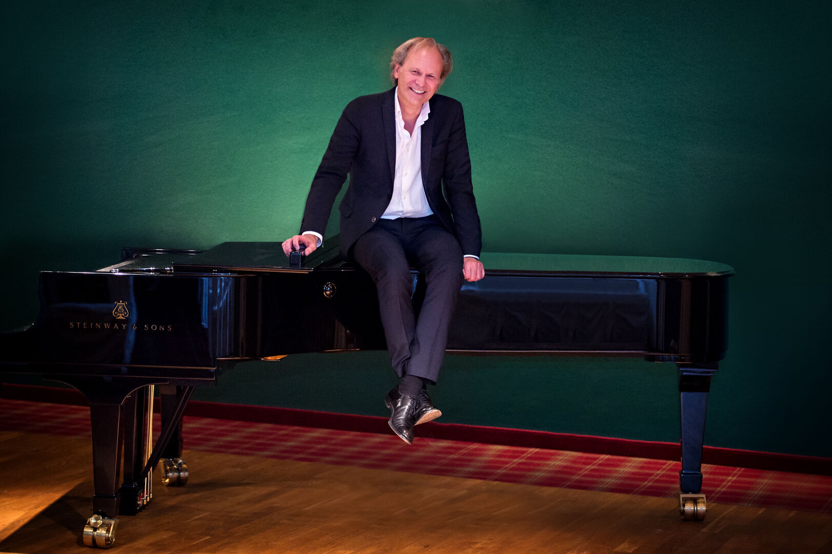 Der künstlerische Leiter des Klangforums Carinthia, Erwin Kropfitsch, sitzt in einen Anzug gekleidet auf einem schwarzen Flügel