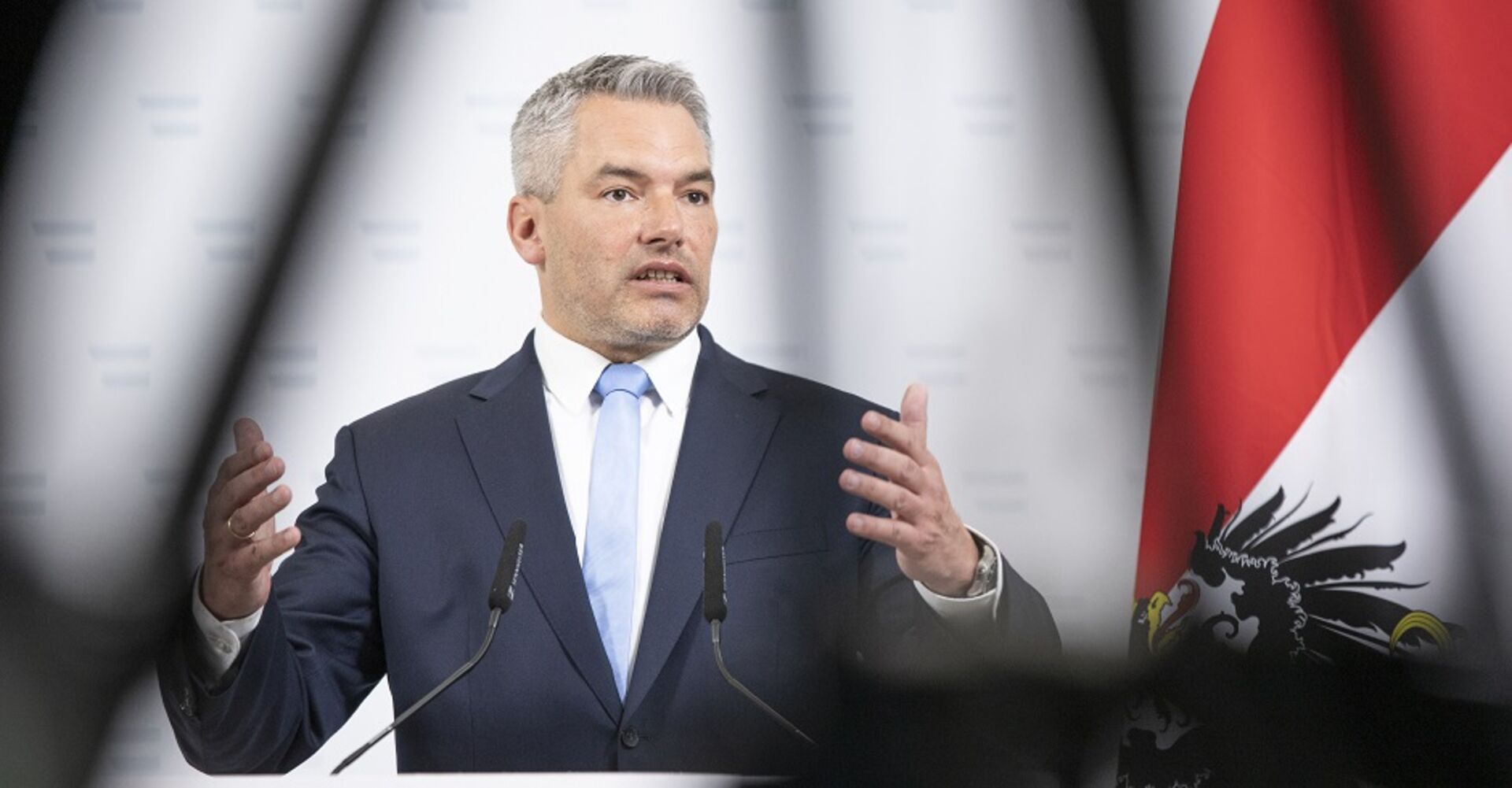 Bundeskanzler Karl Nehammer auf einer Pressekonferenz. Er erklärt etwas. Im Hintergrund die österreichische Flagge