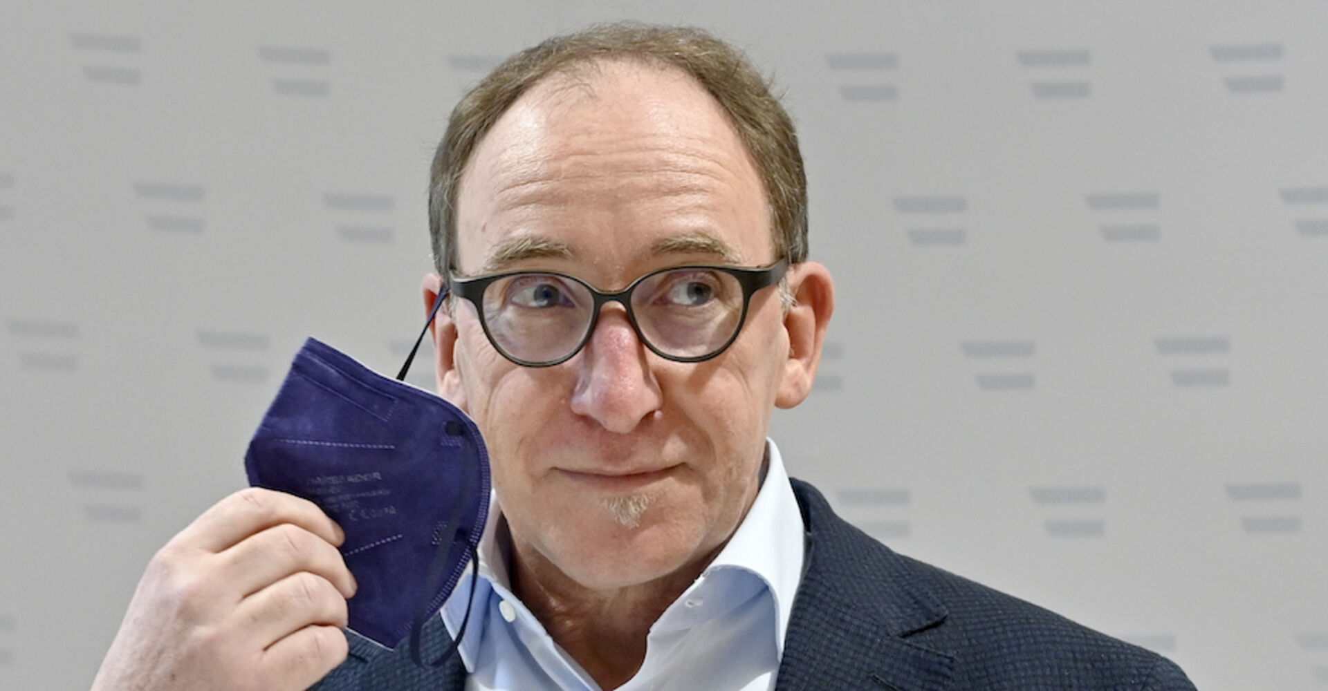 Gesundheitsminister Johannes Rauch bei einer Pressekonferenz. Er nimmt eine violette FFP2-Maske ab