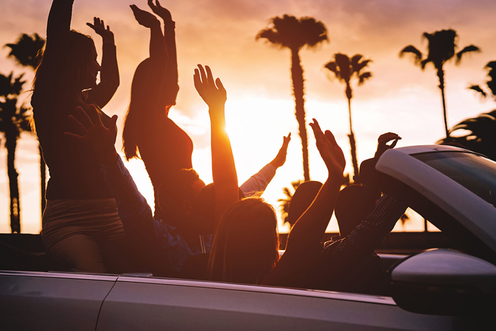 Junge Menschen im Cabrio unterwegs bei Sonnenuntergang | Credit: iStock.com/Alessandro Biascioli