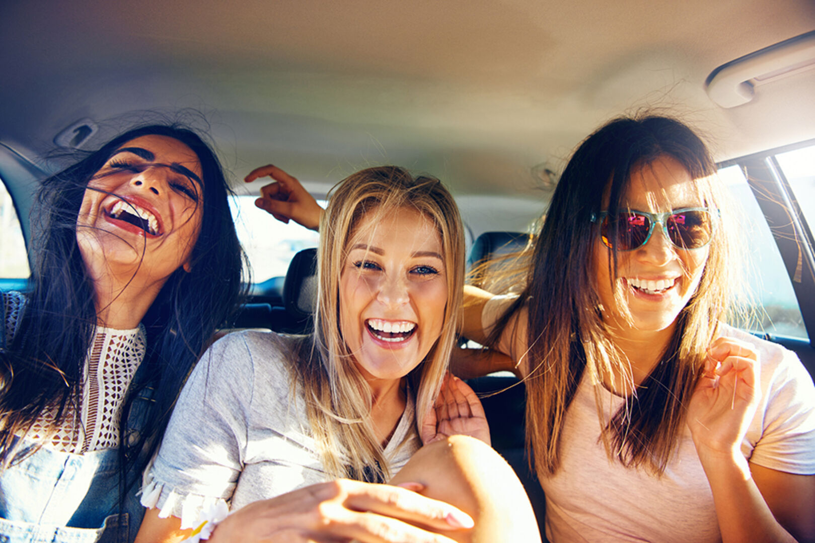 Drei fröhliche junge Frauen zu dritt unterwegs im Auto | Credit: iStock.com/FlamingoImages