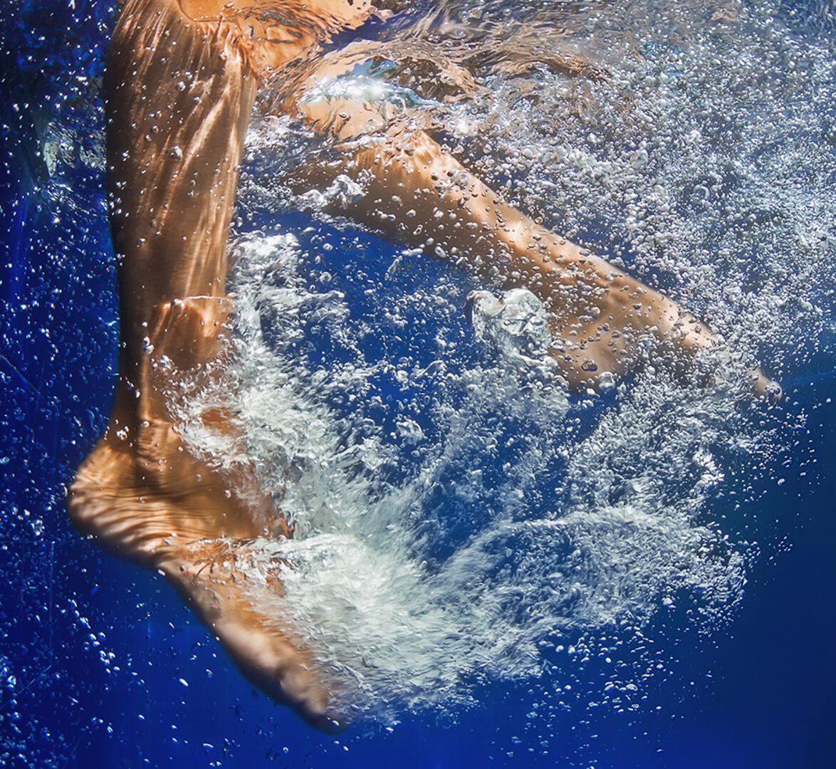 Junge Frau taucht ihre Beine in das Wasser | Credit: iStock.com/Bicho_raro