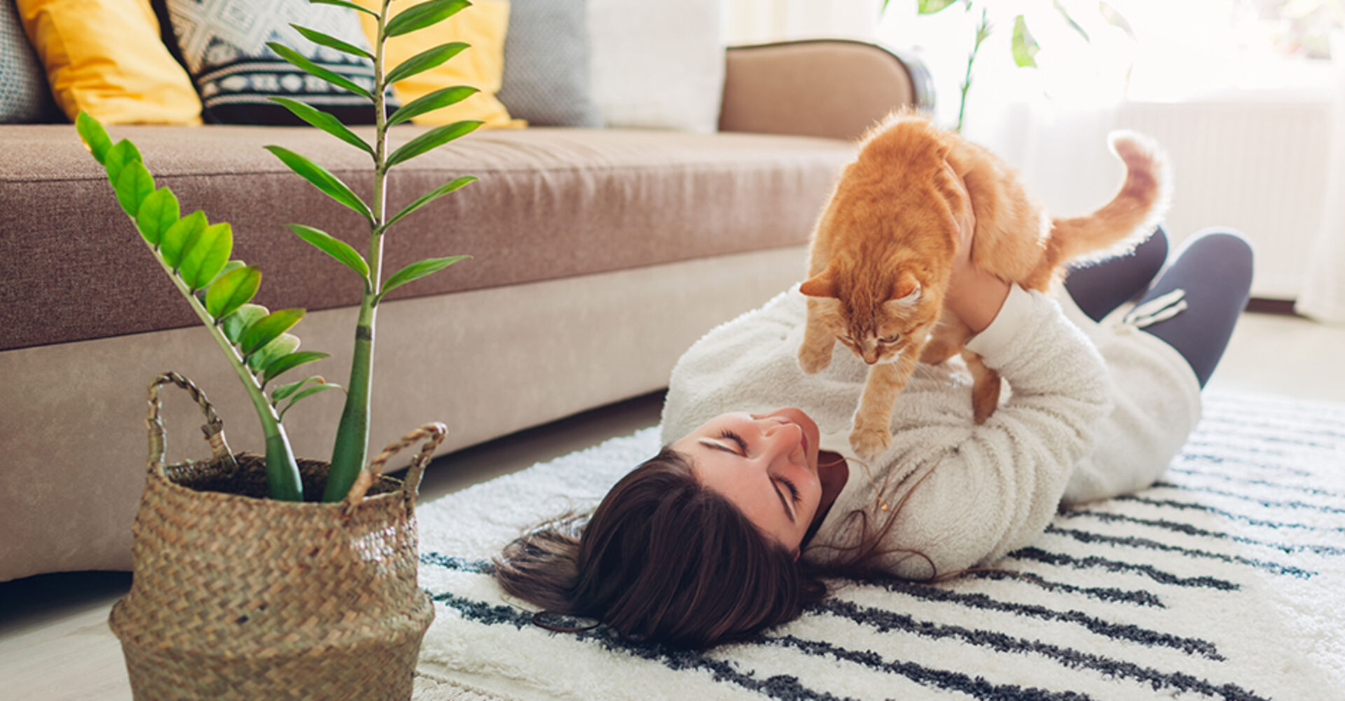 Frau liegt mit ihrer Katze auf dem Teppich ihres gemütlichen Wohnzimmers | Credit: iStock.com/Maryviolet