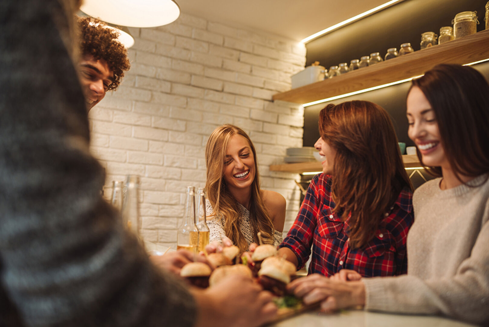 Junge gut gelaunte Frauen und Männer sitzen in der Küche versammelt um den Tisch | Credit: iStock.com/bernardbodo