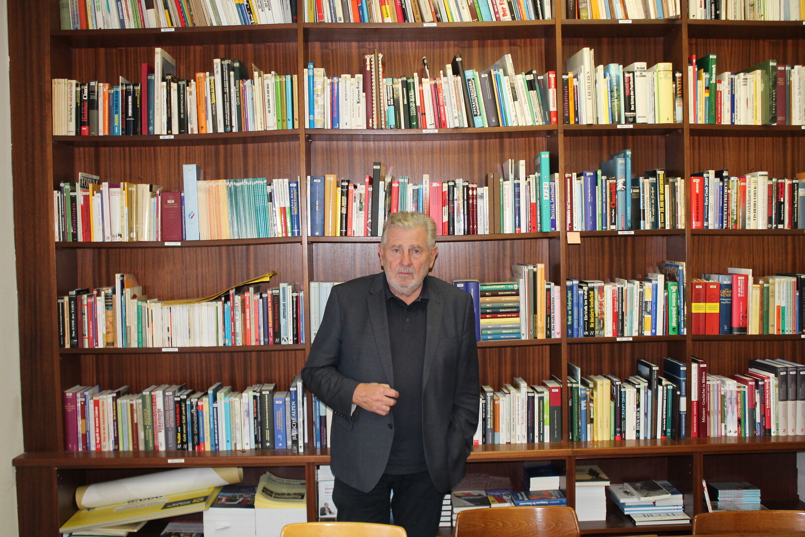 Der Obmann des KHD, Andreas Mölzer, steht vor einem mehrreihigen Bücherregal mit unzähligen Büchern