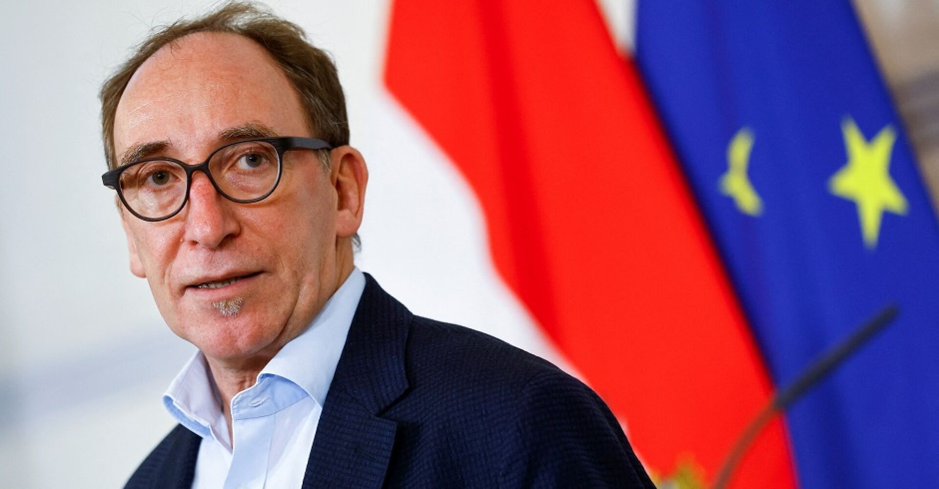 Johannes Rauch mit Brille vor der österreichischen und der europäischen Flagge