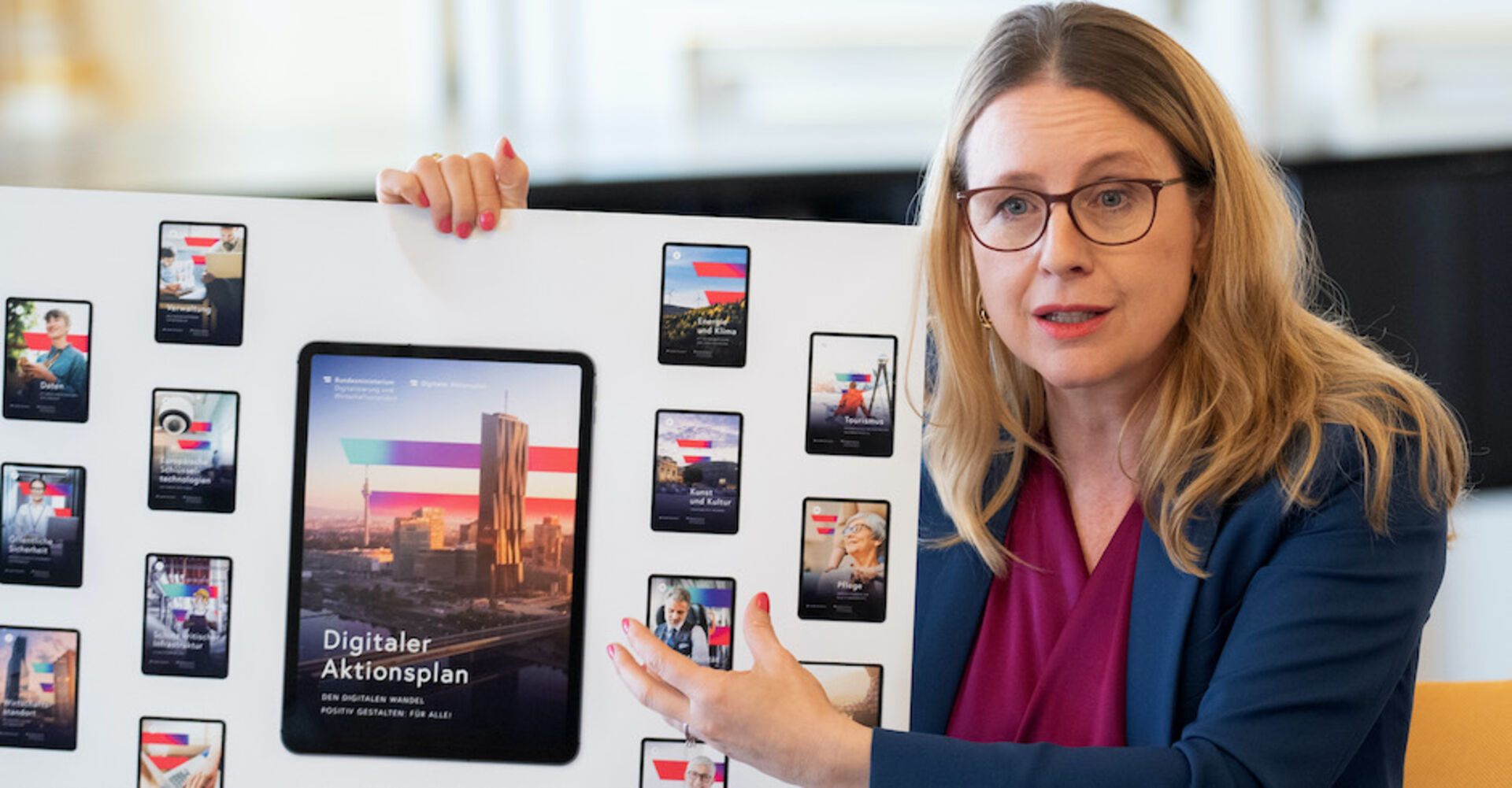 Margarete Schramböck hält einen großformatigen Ausdruck. Darauf zu sehen sind Fotos von Handy- und Tablet-Displays mit dem Slogan &quot;Digitaler Aktionsplan&quot;.
