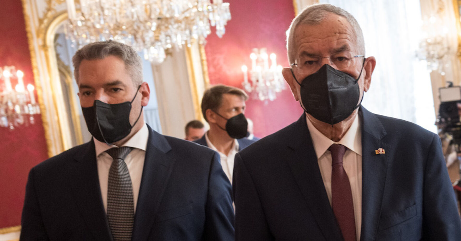 Bundeskanzler Karl Nehammer hinter Bundespräsident Alexander Van der Bellen in der Hofkanzlei. Beide tragen eine schwarze FFP2-Maske