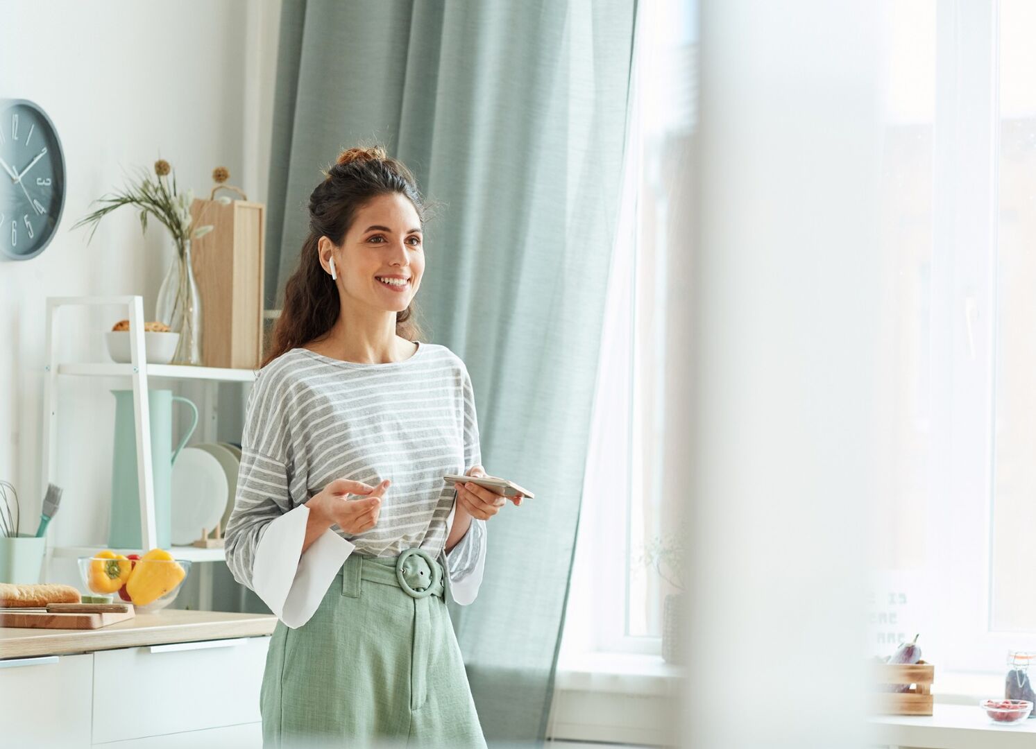 Frau steht vor Fenster mit Gardinen | Credit: iStock.com/SeventyFour