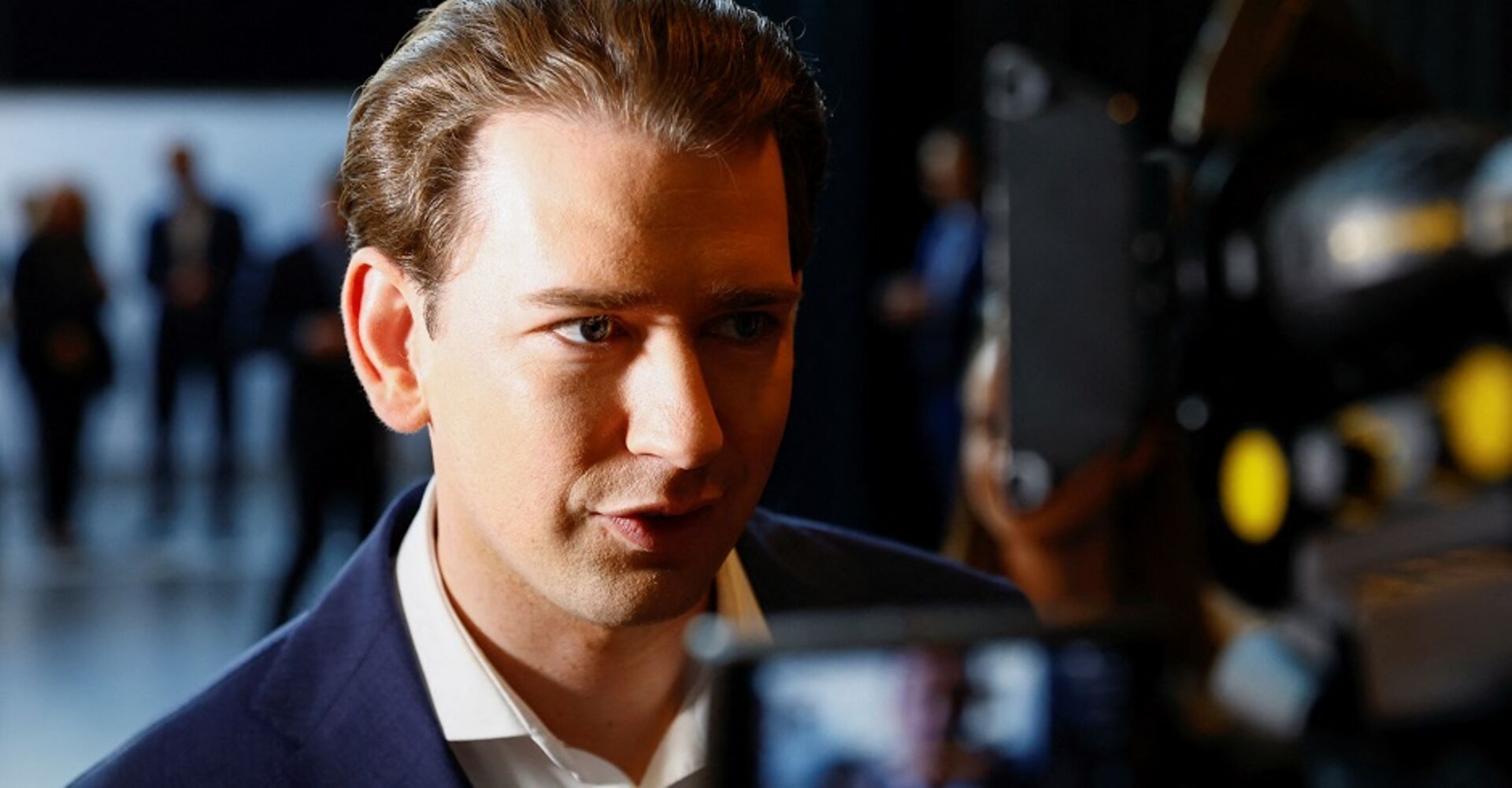 Sebastian Kurz im Halbporträt, sein Gesicht ist nur von einer Seite beleuchtet. Eine Kamera ist auf ihn gerichtet, er gibt ein Interview.