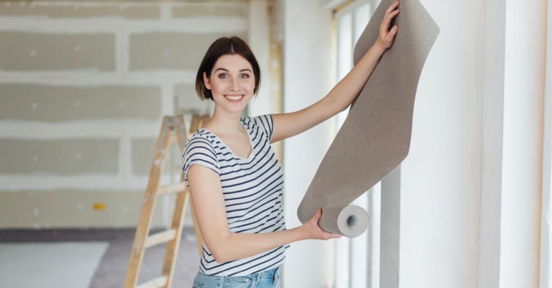 Frau hält eine Tapetenrolle in der Hand | Credit: iStock.com/stockfour