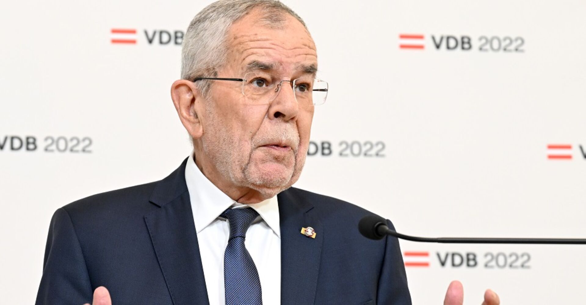 Alexander Van der Bellen bei der Verkündung seiner Wiederkandidatur. Im Hintergrund sein Logo für den Whalkampf: rot-weiß-rote Flagge VDB 2022. Er wirkt ratlos