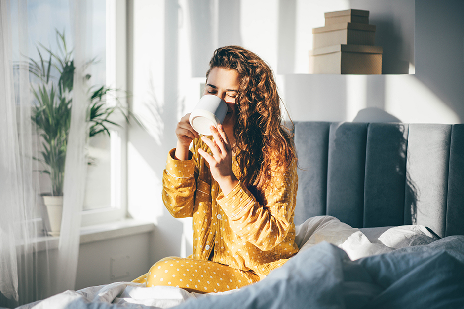 Junge ausgeruhte Frau genießt ihren Morgenkaffee im Bett | Credit: iStock.com/Maria Korneeva
