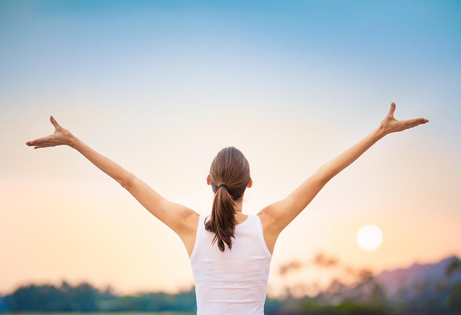 Junge Frau streckt ihre Arme in der Morgensonne seitlich in die Höhe | Credit: iStock.com/kieferpix