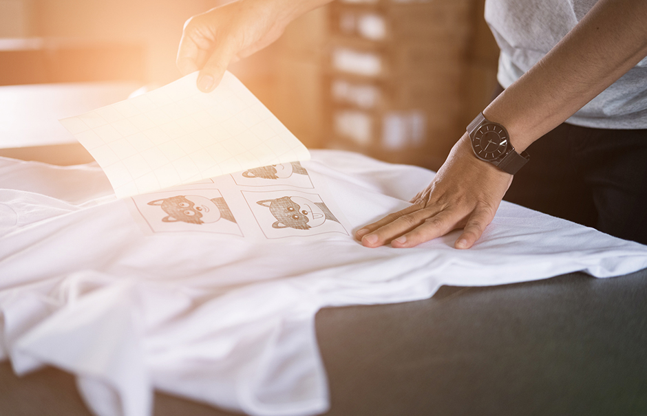 Junger Mann bügelt ein Motiv auf sein weißes T-Shirt auf | Credit: iStock.com/psisa