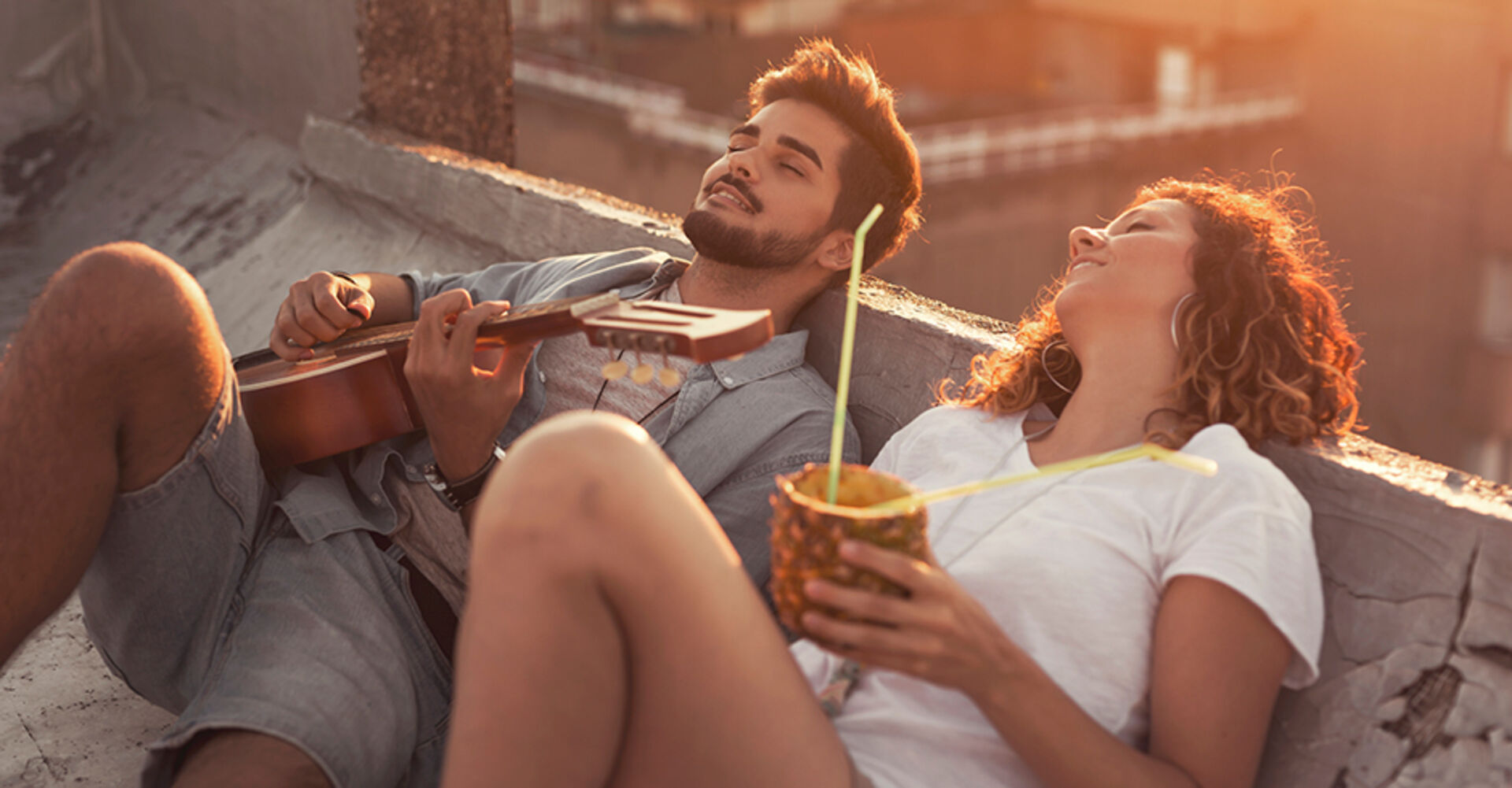 Junge glückliches Pärchen an einem lauen Sommerabend auf der Terrasse über den Dächern der Stadt | Credit: iStock.com/vladans