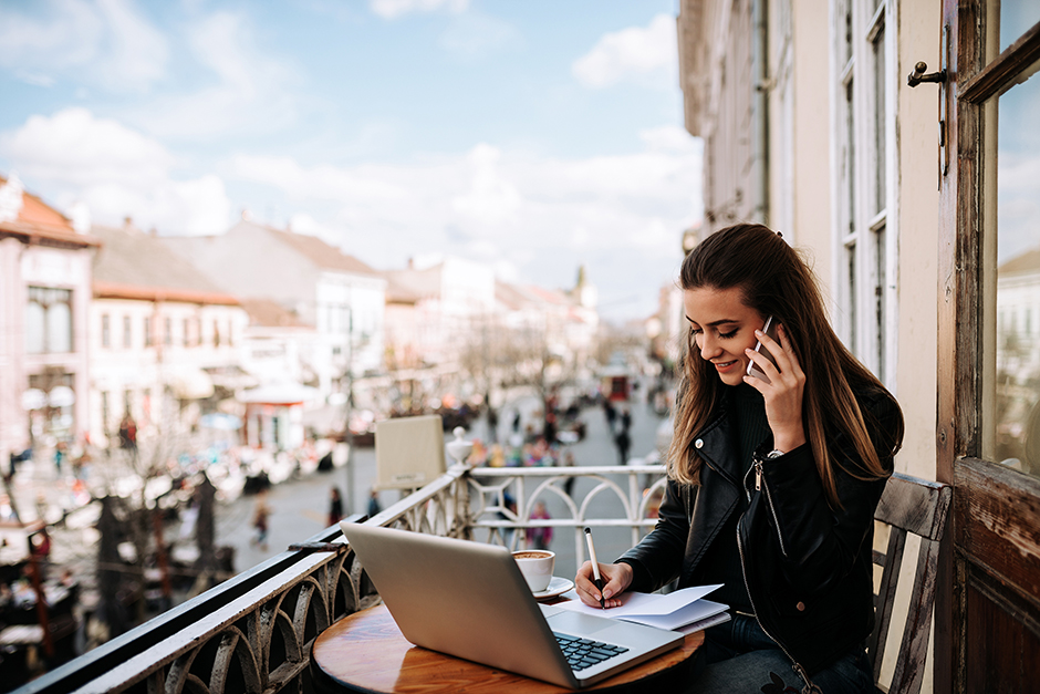 Junge Frau im Home Office auf dem Balkon ihrer Altbauwohnung im Stadtzentrum | Credit: iStock.com/nortonrsx