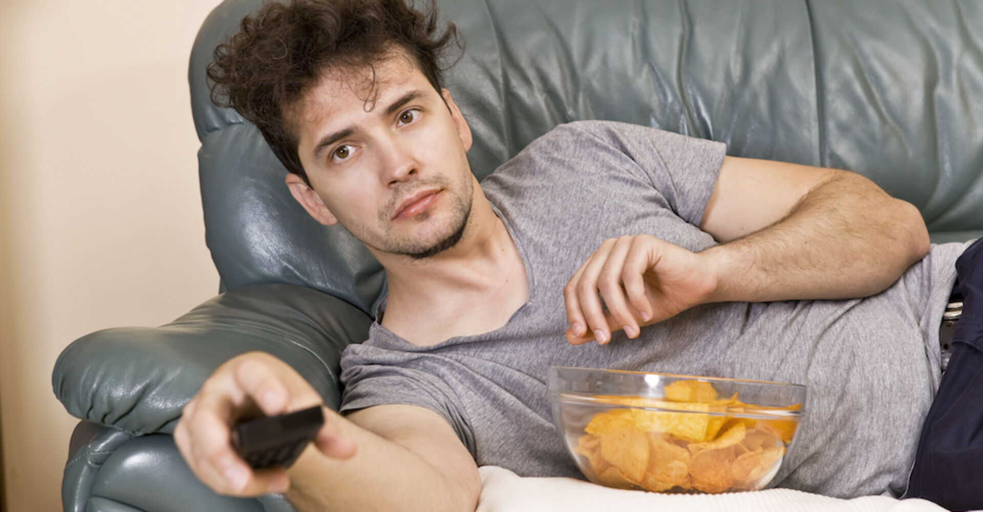 Mann liegt faul auf der Couch und schaut fern | Credit: iStock.com/lukas_zb