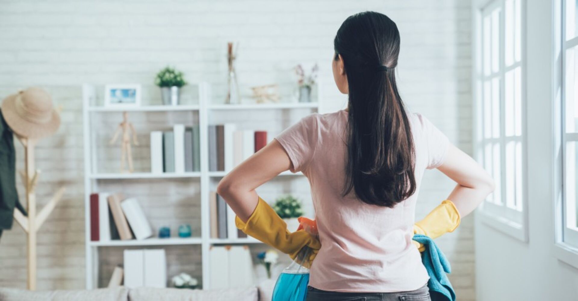 Frau steht mit Putzutensilien im Wohnzimmer | Credit: iStock.com/PRImageFactory