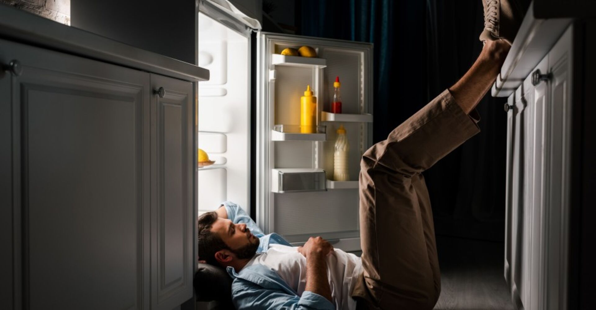 Mann liegt am Boden vor offenem Kühlschrank | Credit: iStock.com/LightFieldStudios