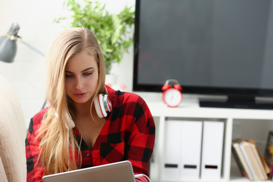 Junge Frau mit Kopfhörern um ihren Hals vor ihrem Computer | Credit: iStock.com/Ivan-balvan