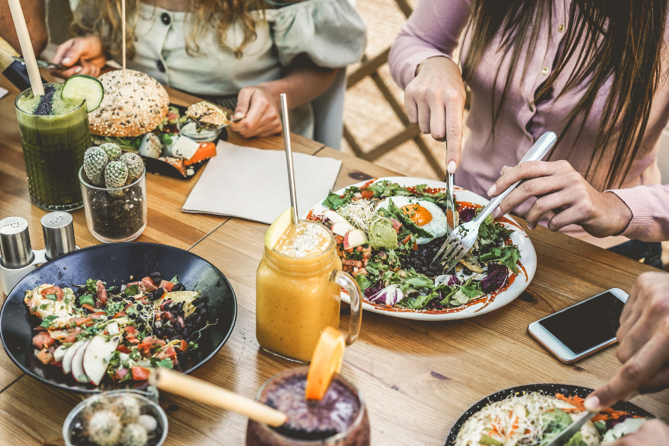 Runde junger Frauen und Männer beim gemeinsamen Essen | Credit: iStock.com/DisobeyArt