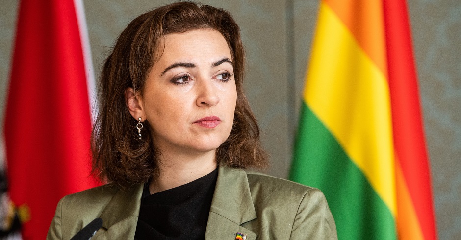 Alma Zadic vor der österreichischen und der Regenbohnenfahne.